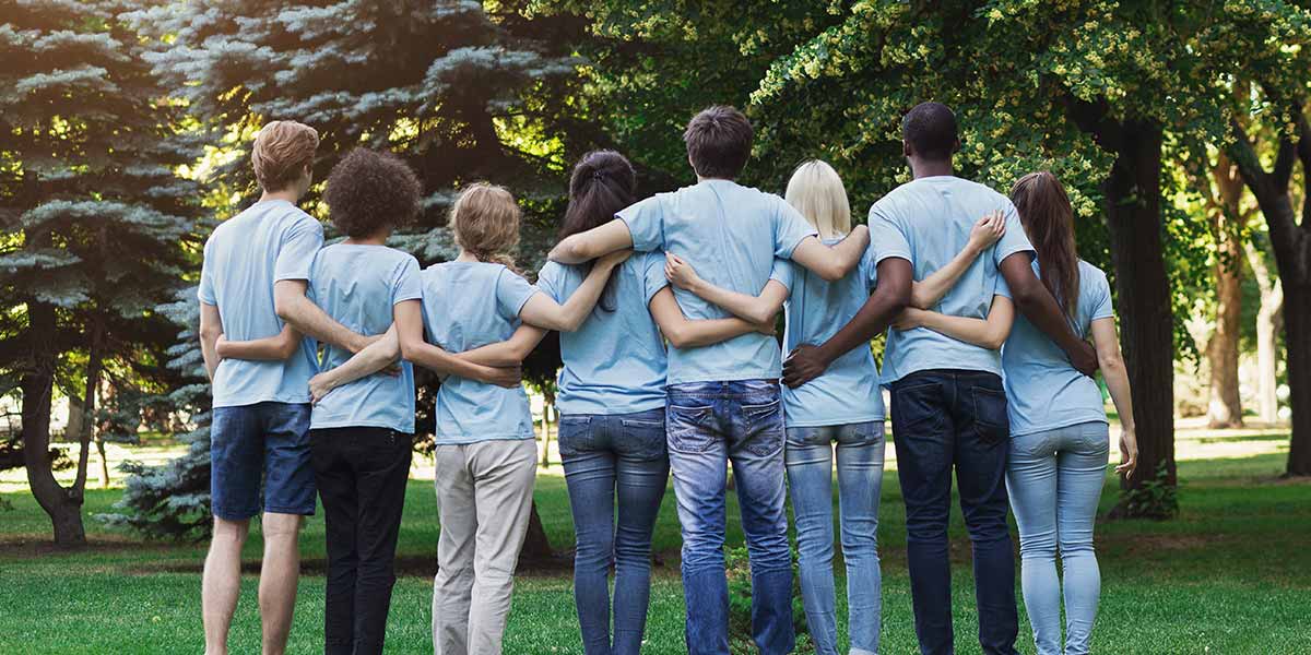 Photo of a group of volunteers in blue shirts standing with their arms around each other, facing away from the camera