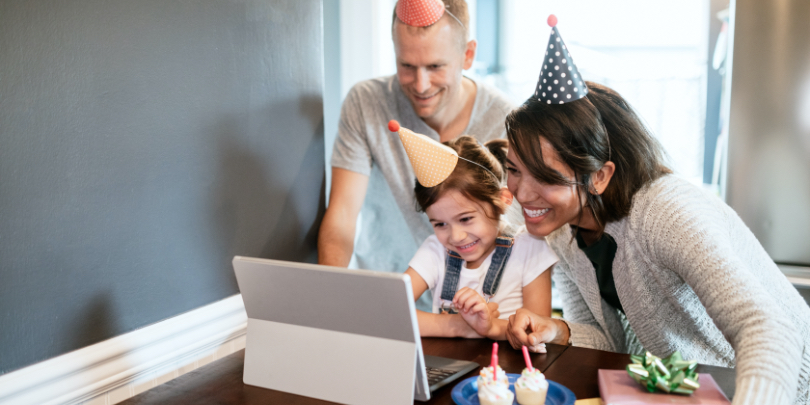 photo of parents with small girl wearing birthday hats and smiling looking at a computer