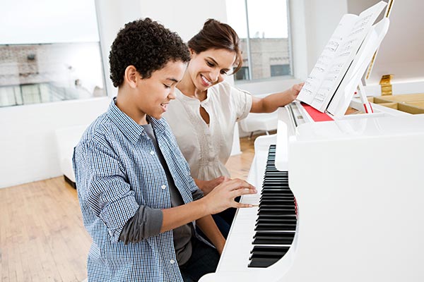 piano teacher sitting with student at piano teaching music lessons