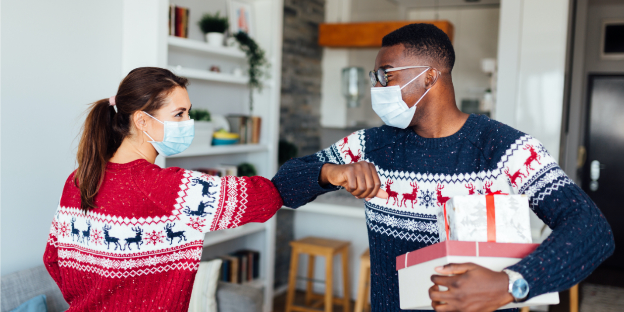 photo of two friends inside with masks holding Christmas gifts and bumping elbows