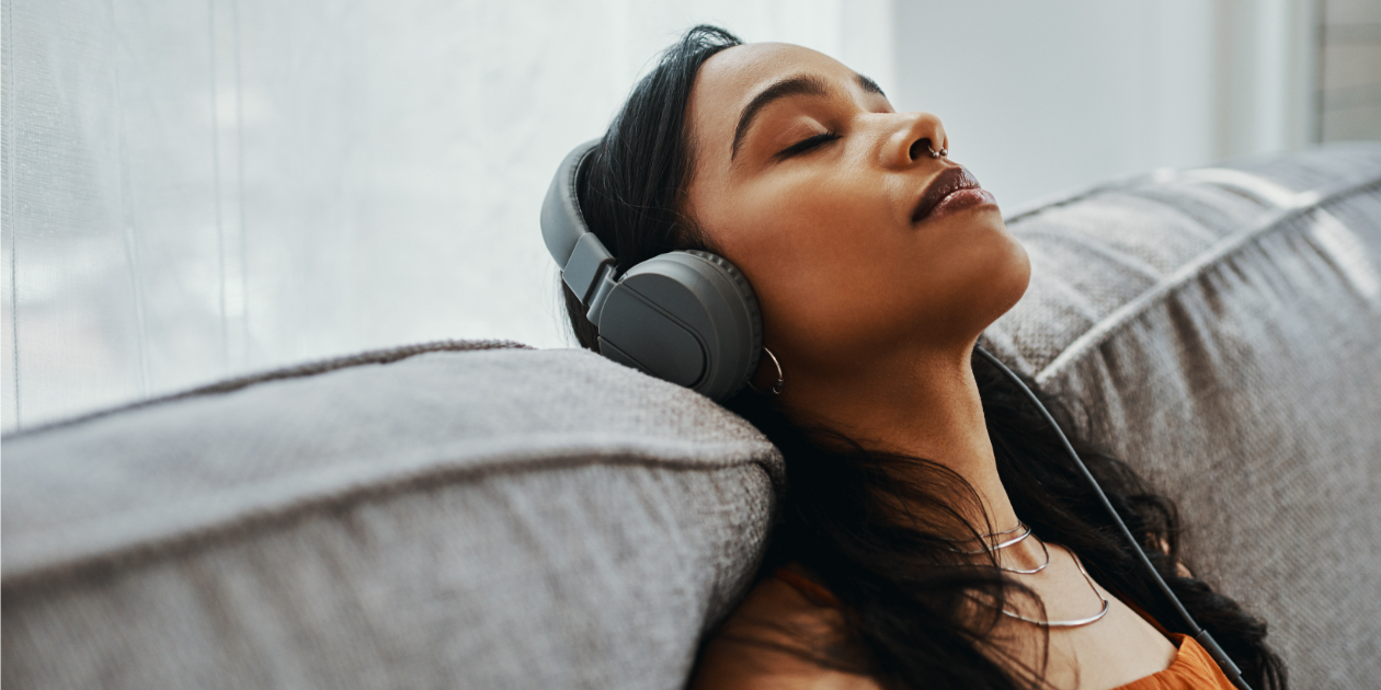 photo of woman sitting on a couch listening to music on headphones