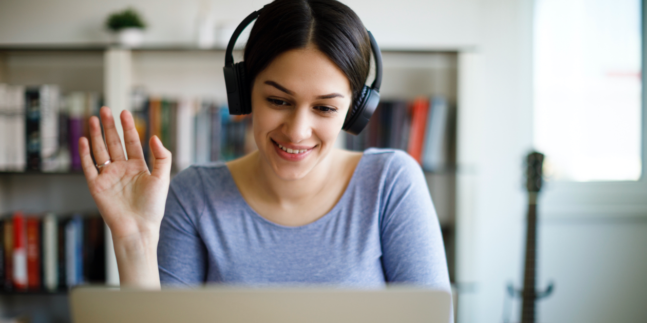 photo of woman with headphones waving at a laptop